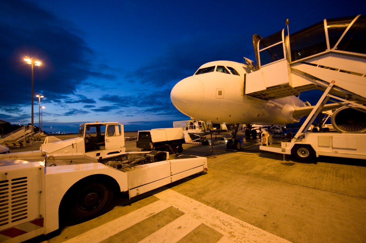 Aircraft being serviced on the apron at dusk with ground-support equipment.