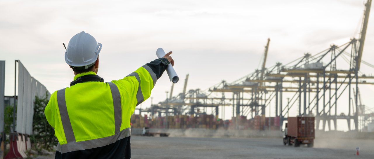 Hi-vis logistics planner directing operations at a container terminal, seen from behind.