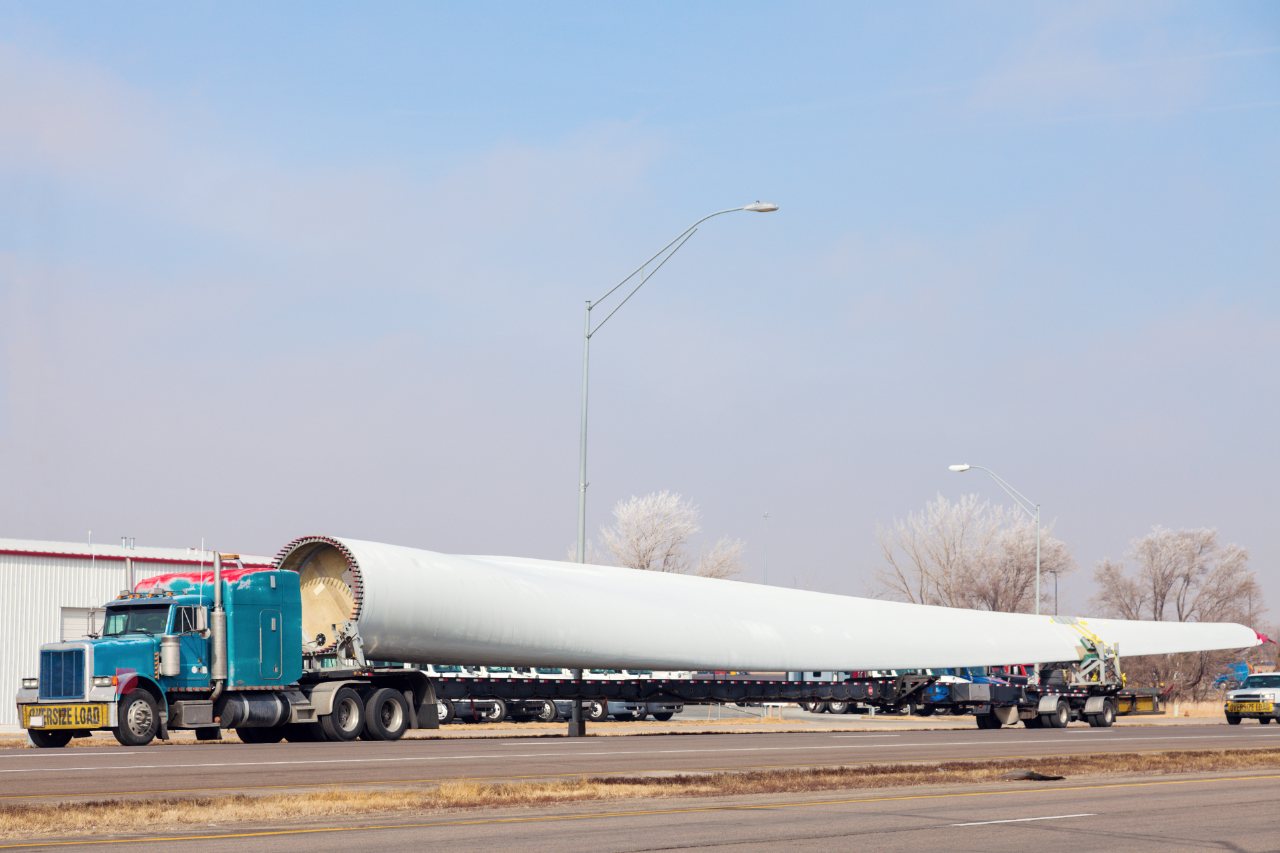 Semi truck hauling an oversized wind-turbine blade on an extendable flatbed trailer marked OVERSIZE LOAD